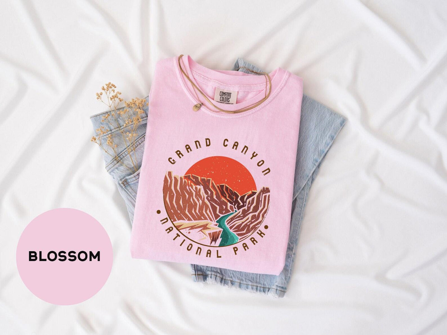 a pink shirt with a bird on it sitting on top of a pair of jeans