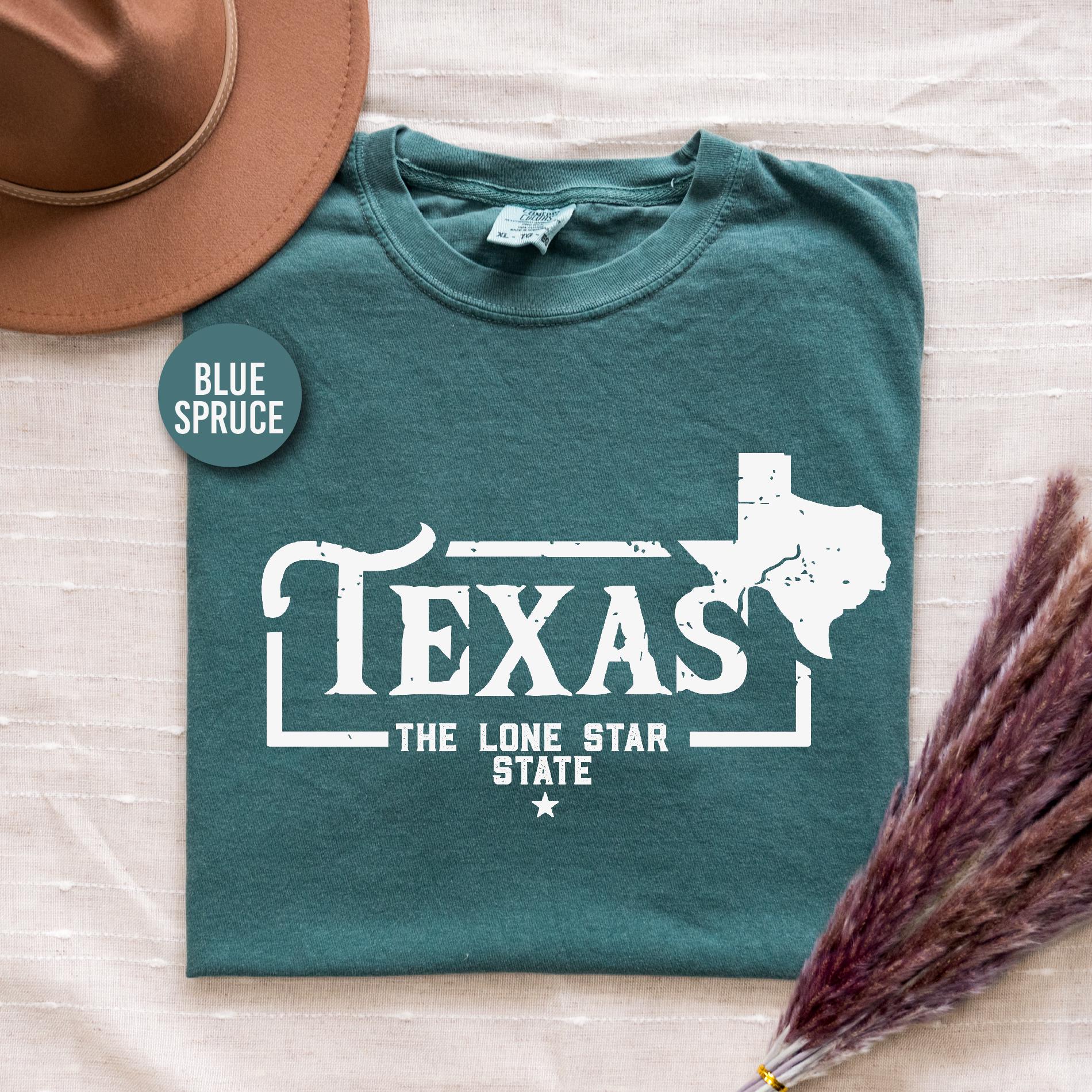 a t - shirt that says texas the lone star state sits next to a hat