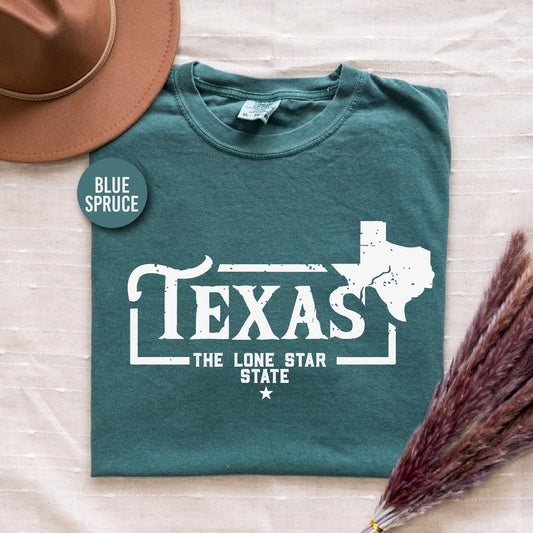 a t - shirt that says texas the lone star state sits next to a hat