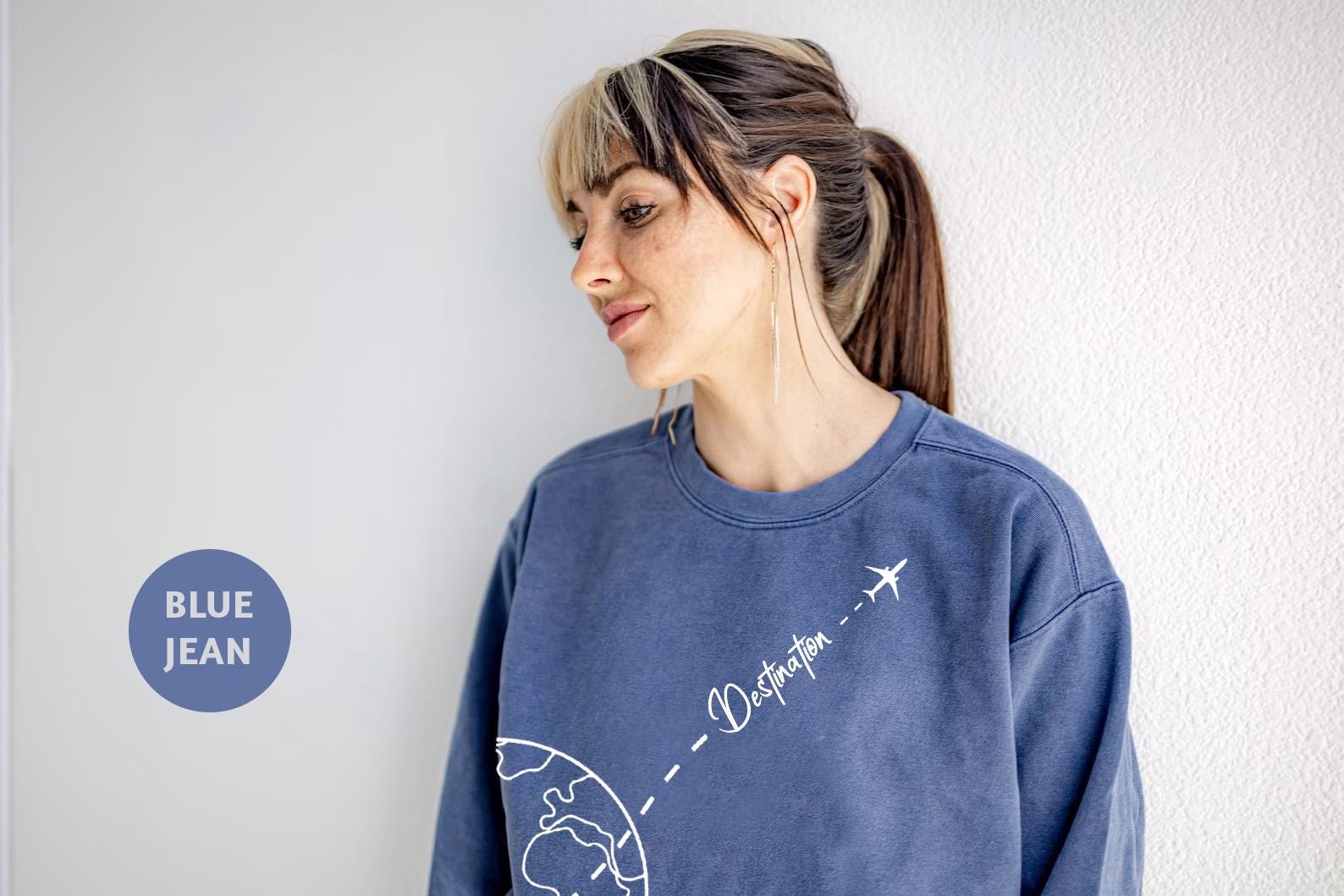 a woman standing against a wall with a blue jean sweatshirt on