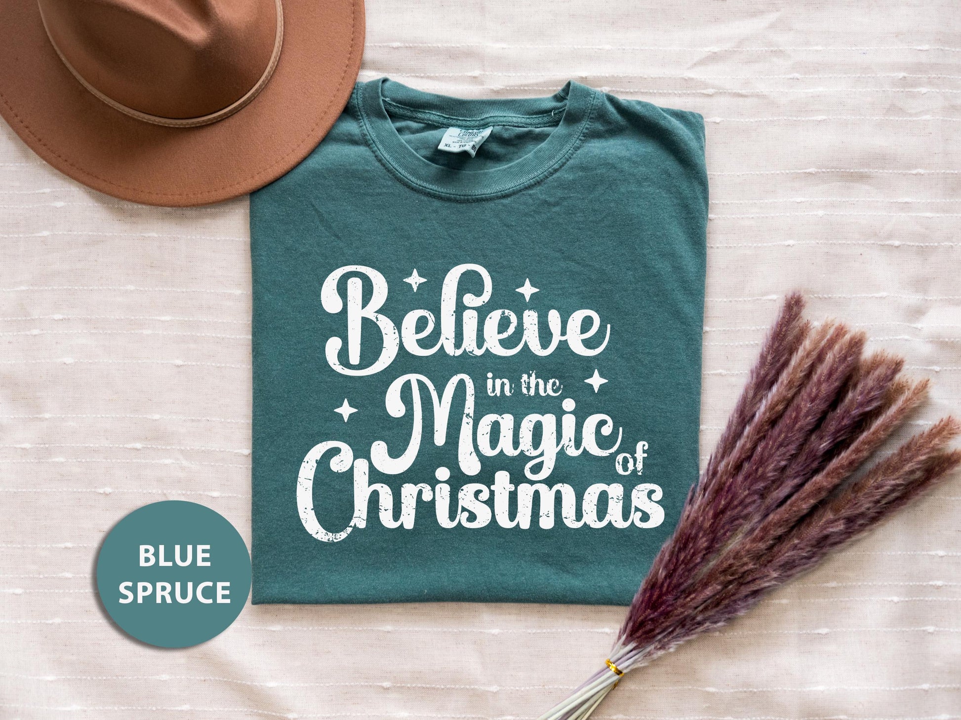 a t - shirt that says believe in the magic of christmas next to a hat