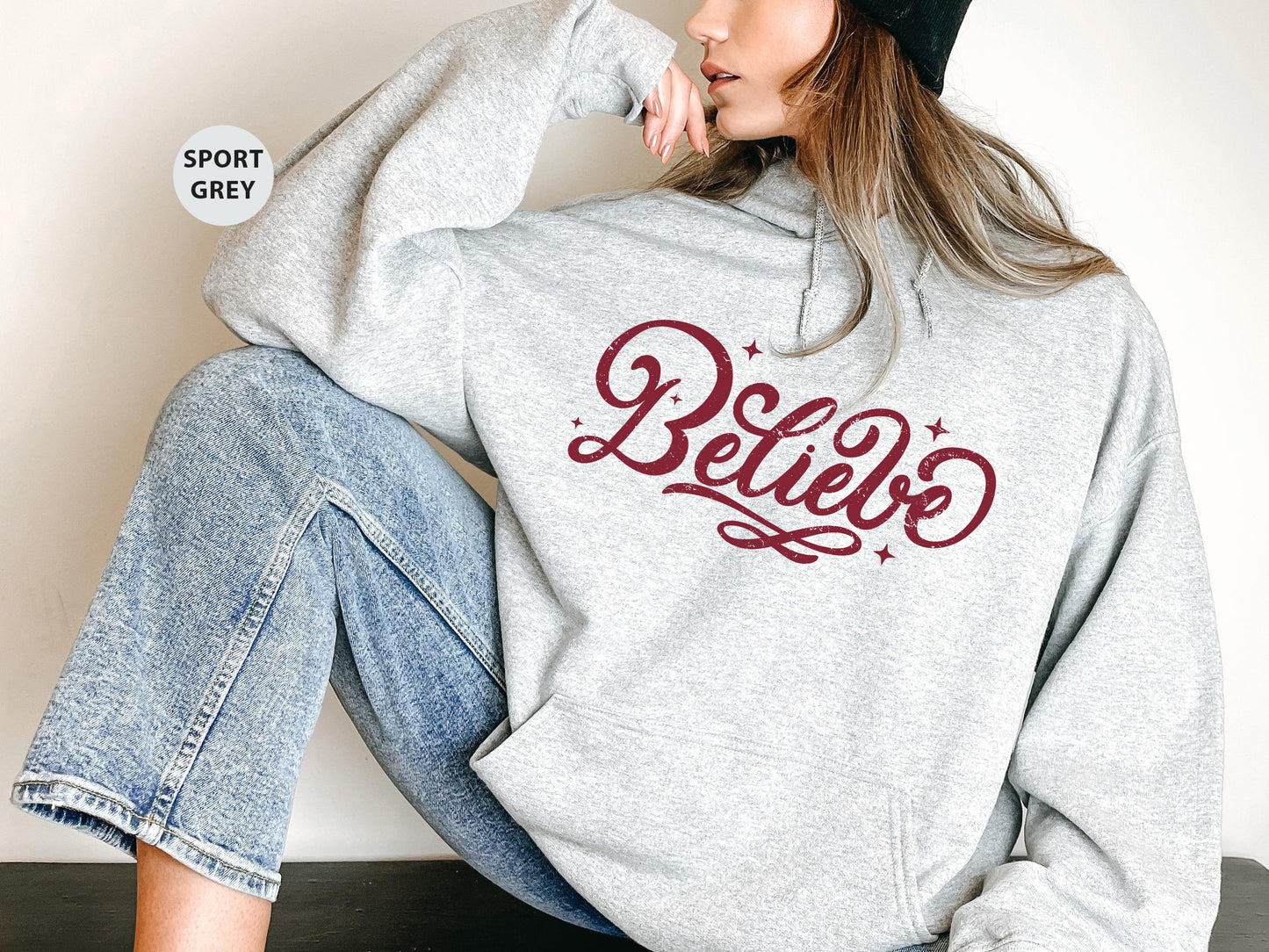 a woman sitting on the ground wearing a sweatshirt and jeans