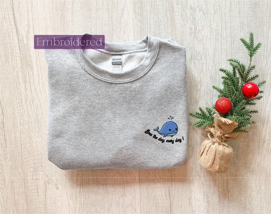 a gray sweatshirt with a blue whale embroidered on it next to a small christmas tree