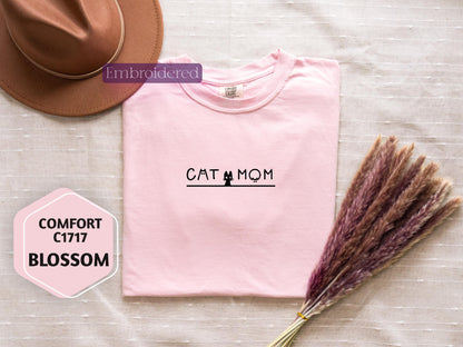 a pink shirt with a cat mom on it next to a hat