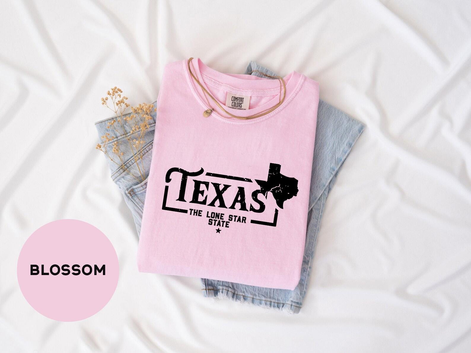 a pink texas t - shirt sitting on top of a pair of jeans