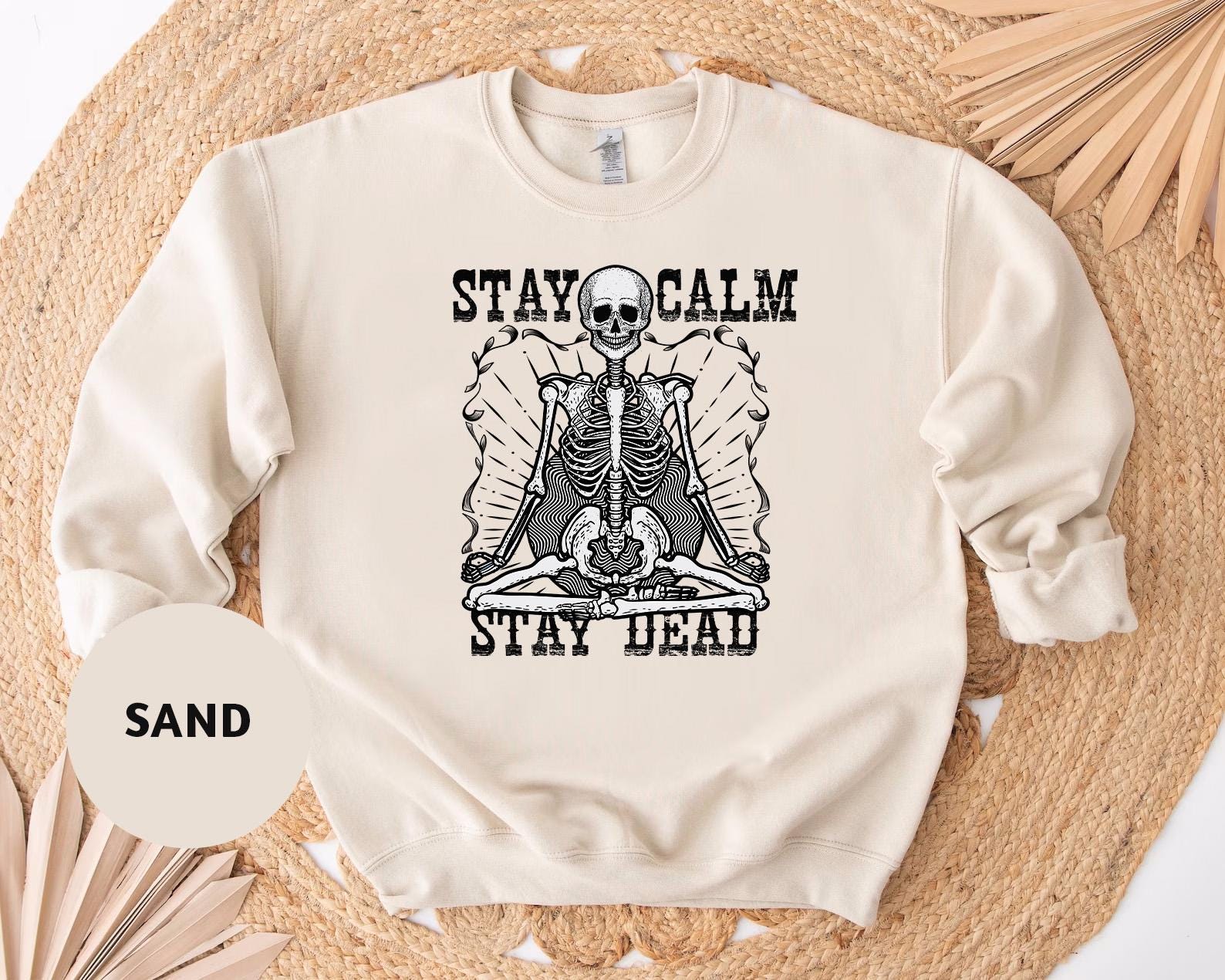 a white sweatshirt with a skeleton on it saying stay calm and stay dead