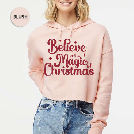 a woman wearing a pink hoodie that says believe in the magic of christmas