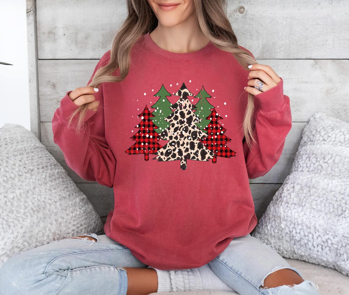a woman sitting on a bed holding up a christmas tree sweatshirt